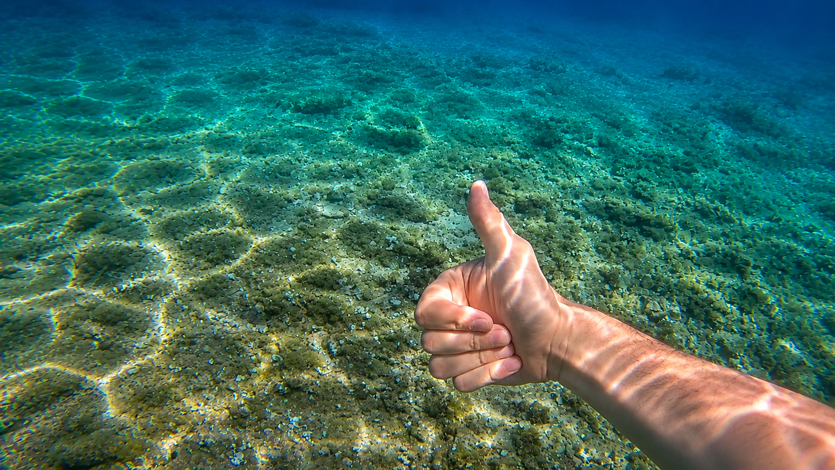 Underwater thumbs up above a pebble seabed
