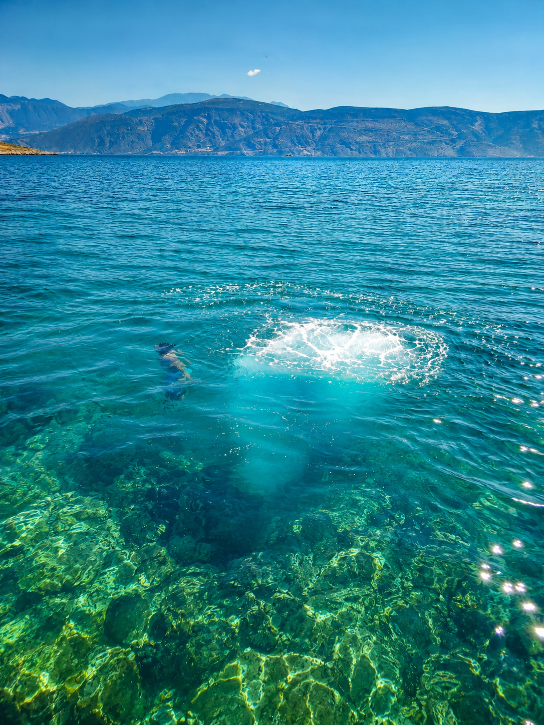 Swimmer in crystal clear turquoise water with mountains behind