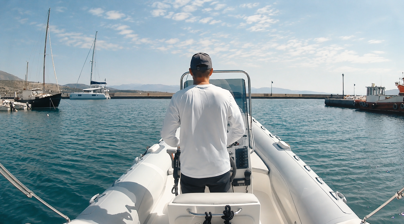 Skipper at the helm leaving Itea harbour past moored sailboats